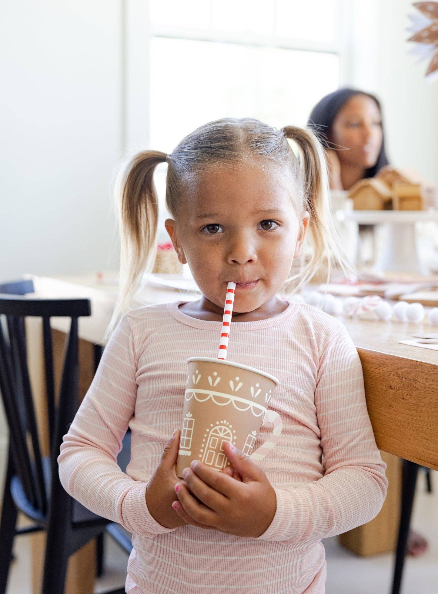 Gingerbread house design cup with pink and white strip paper handle. Girl sipping on pink and wite strip straw